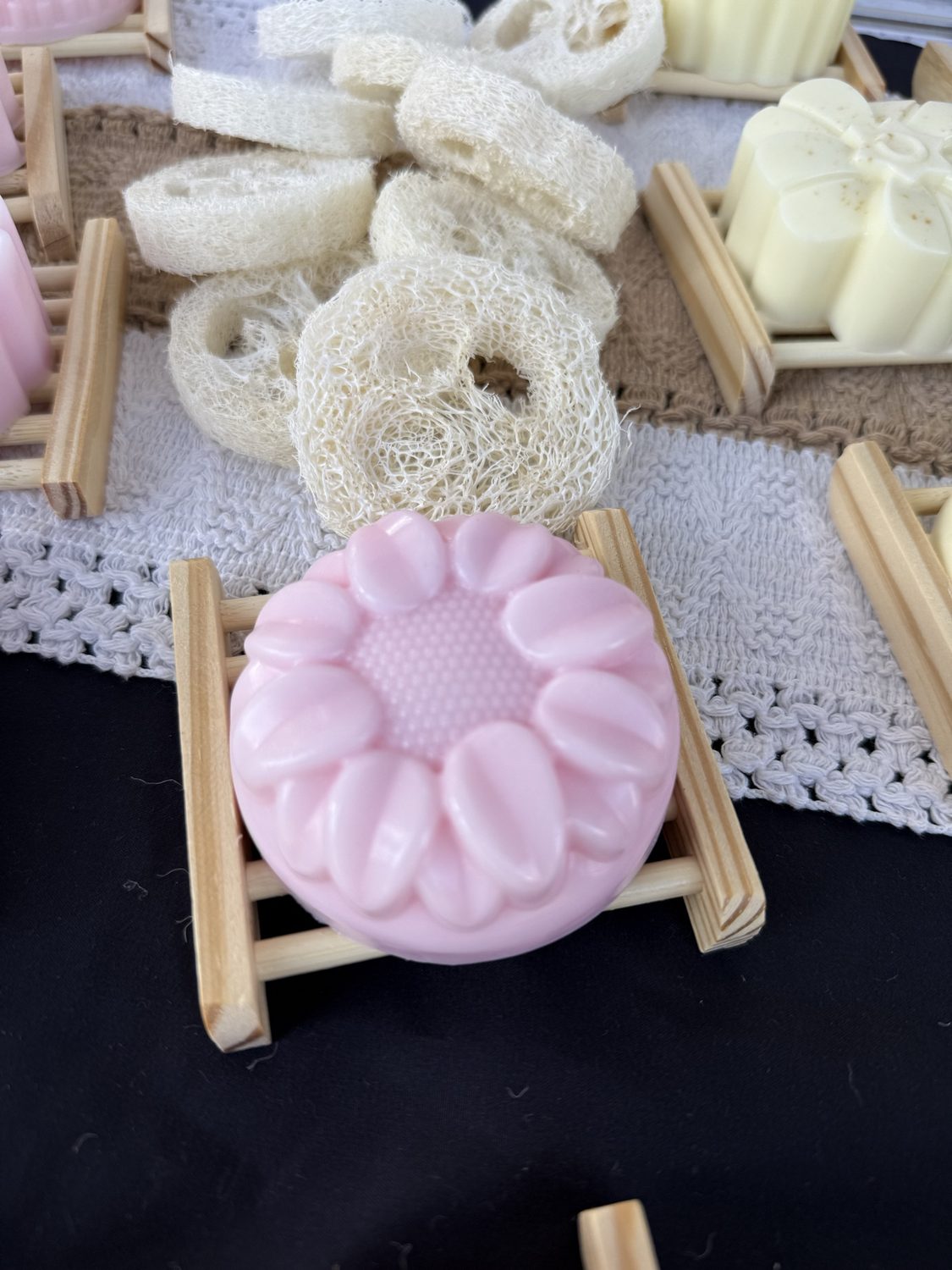 Round pale pink soap molded with a sunflower design on a wood dish