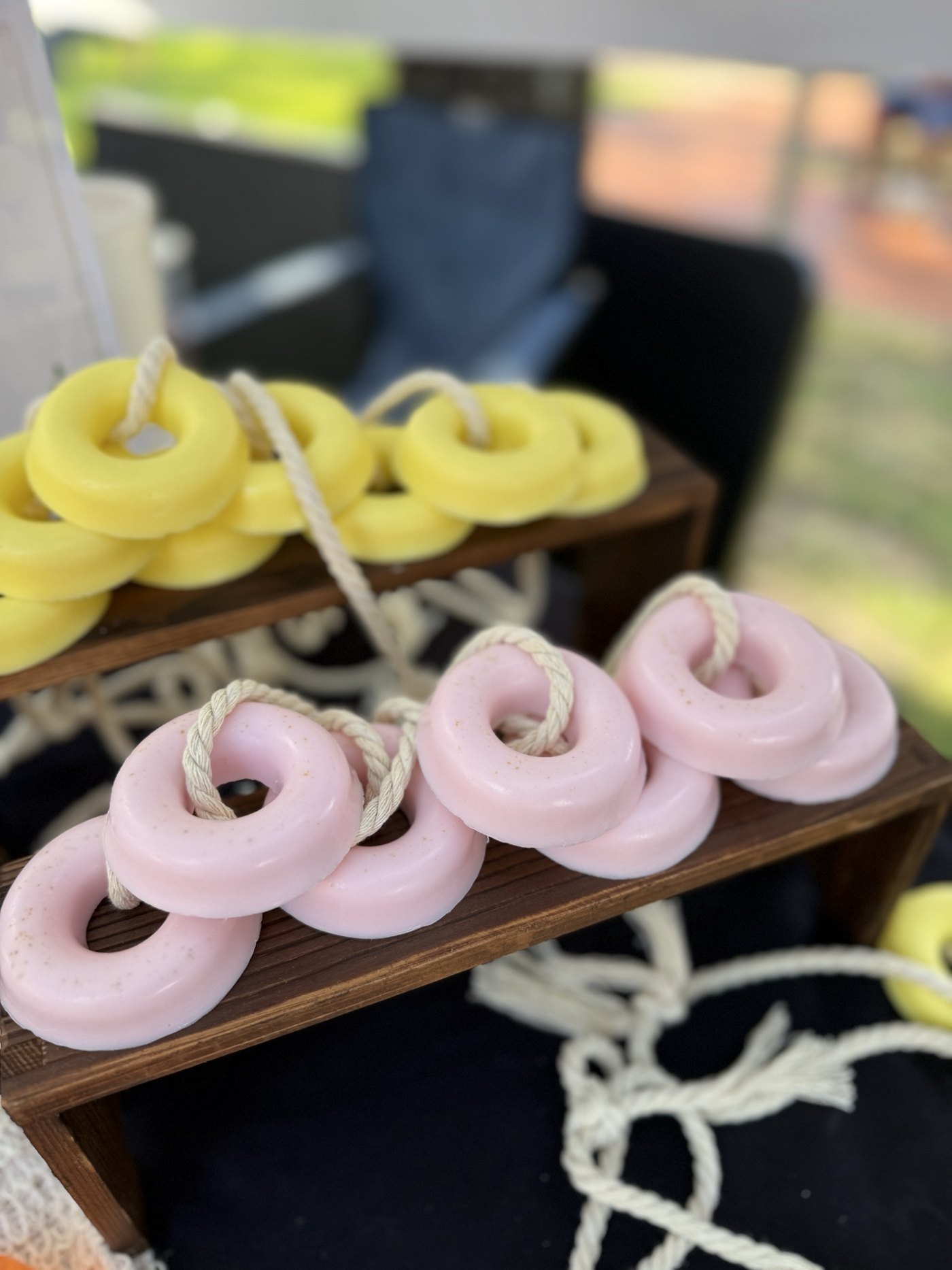 Pink and yellow handmade candles arranged on a wooden display stand