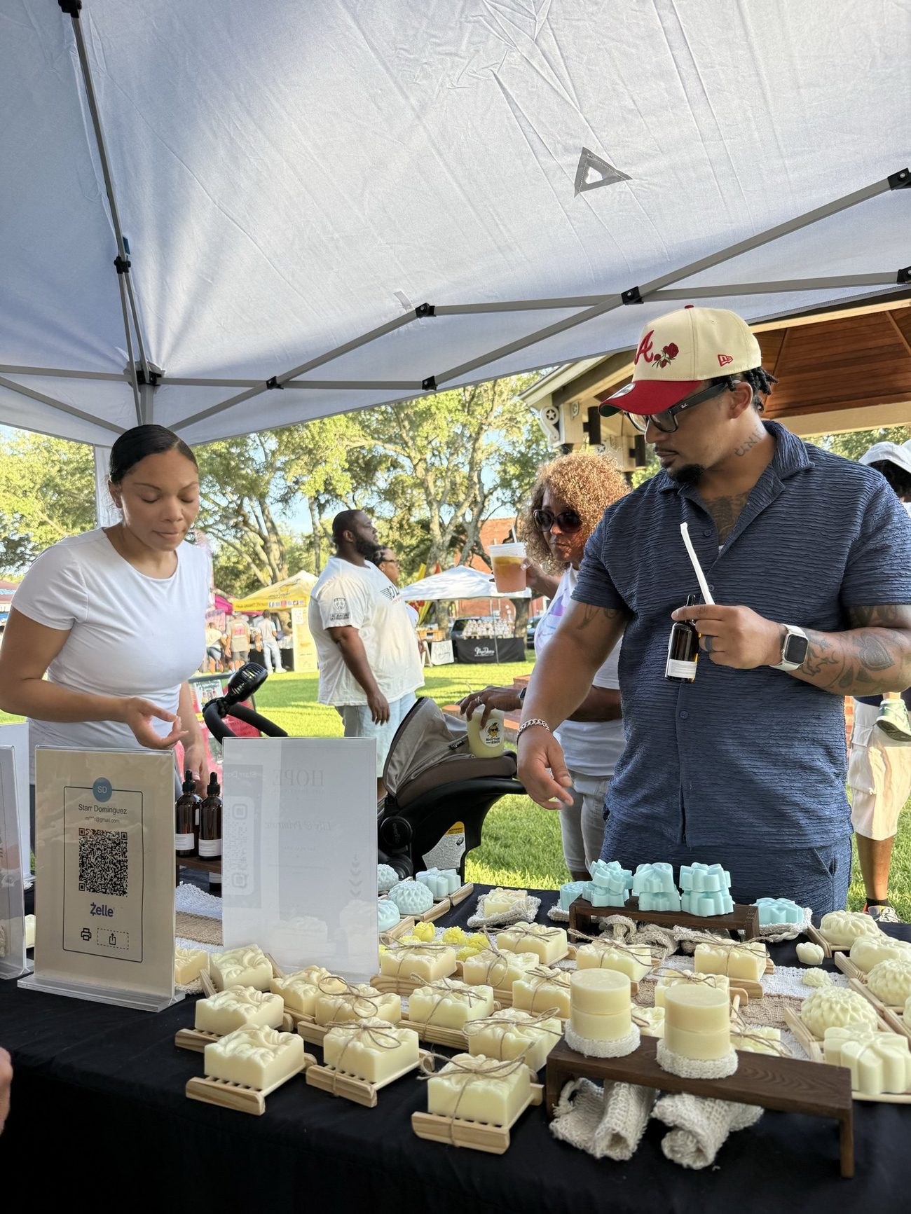 Shoppers browsing a table of handmade soaps under a tent at an outdoor market